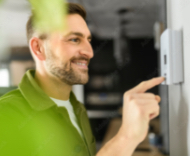 Lächelnder Mann stellt an einem Smart-Home-Thermostat eine Einstellung ein.